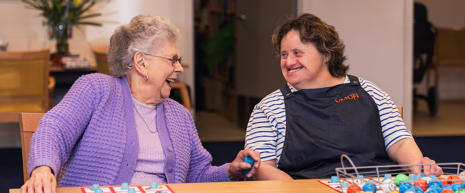 Two women sit at a table and smile at each other